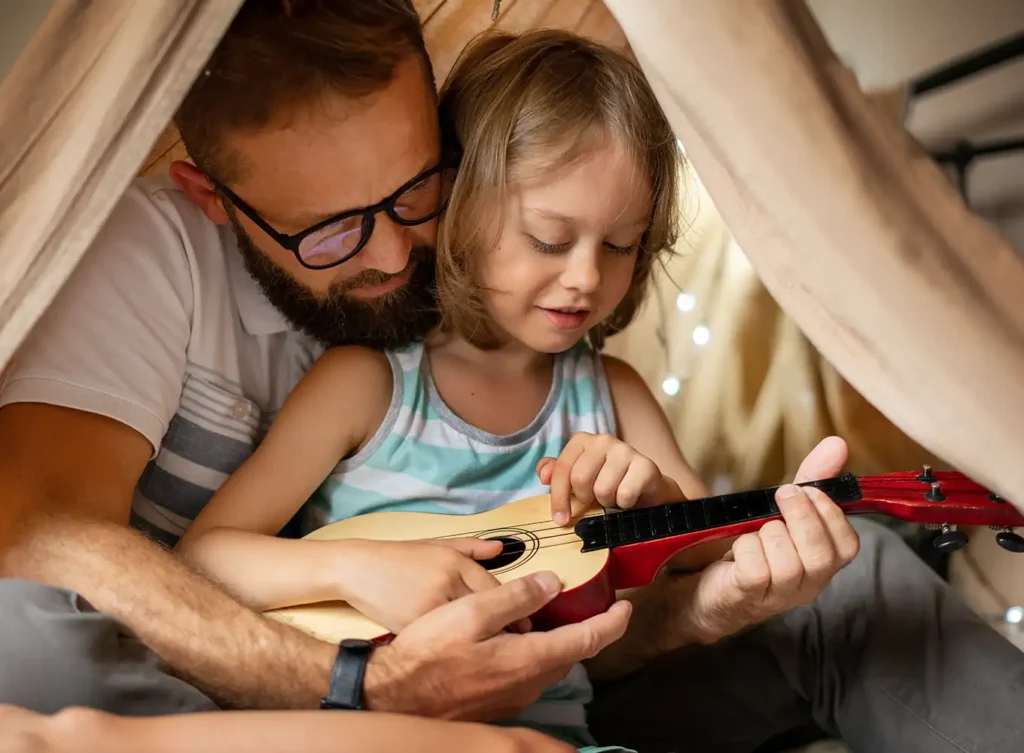 father and child playing a ukulele under a tent in their home springfield il